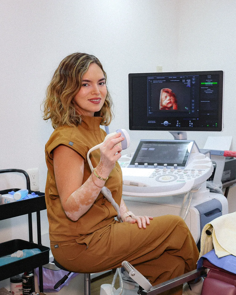 La Dra. Doris Castillo sonríe sentada junto al equipo de ultrasonido de su consultorio